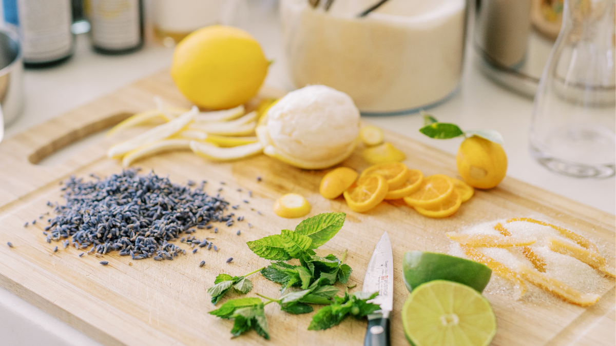Wooden cutting board with lemons, lavender, and herbs on a kitchen counter.