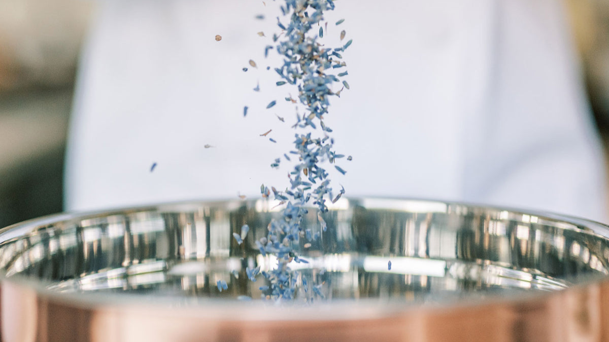 Chef pouring fresh lavender flowers into a copper mixing bowl