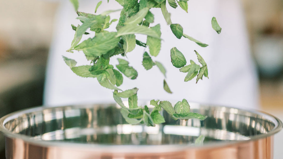 Fresh mint leaves falling into a copper pot
