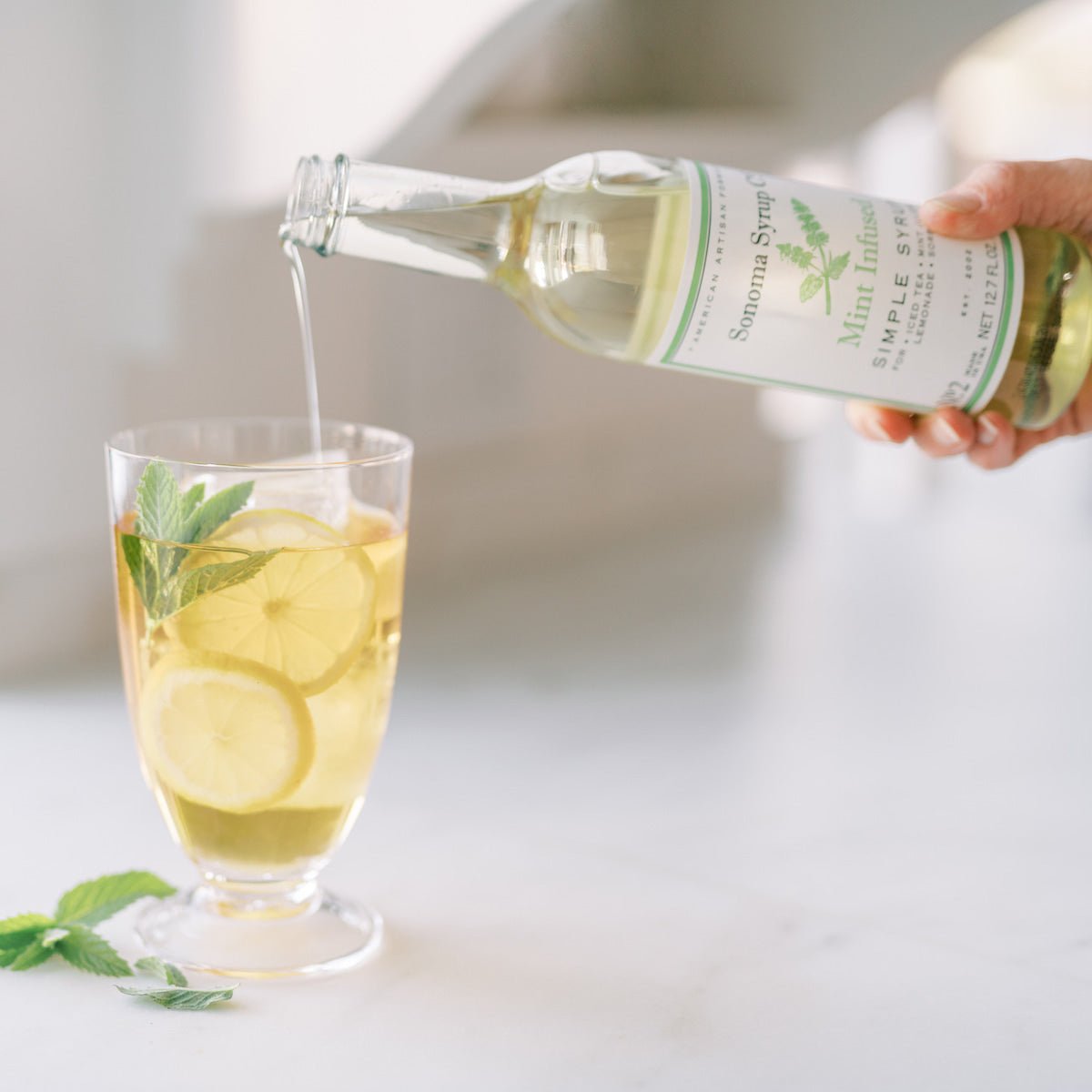 Mixologist pouring Botanical Infused Gift Box - Sonoma Syrup Co. into cocktail glass with lemons and mint